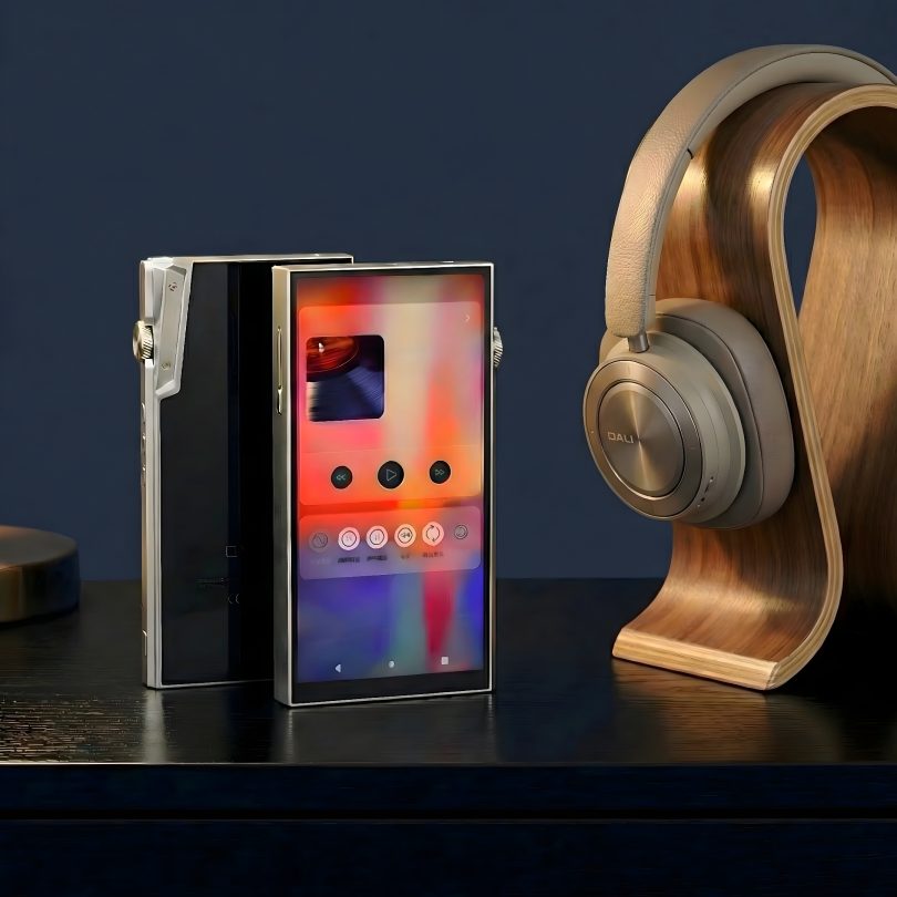 Deux baladeurs audiophiles iBasso DX340 en finition titane posés sur un bureau sombre à côté d'un casque audio DALI sur un support en bois, mettant en avant l'écran tactile et le design métallique brossé.