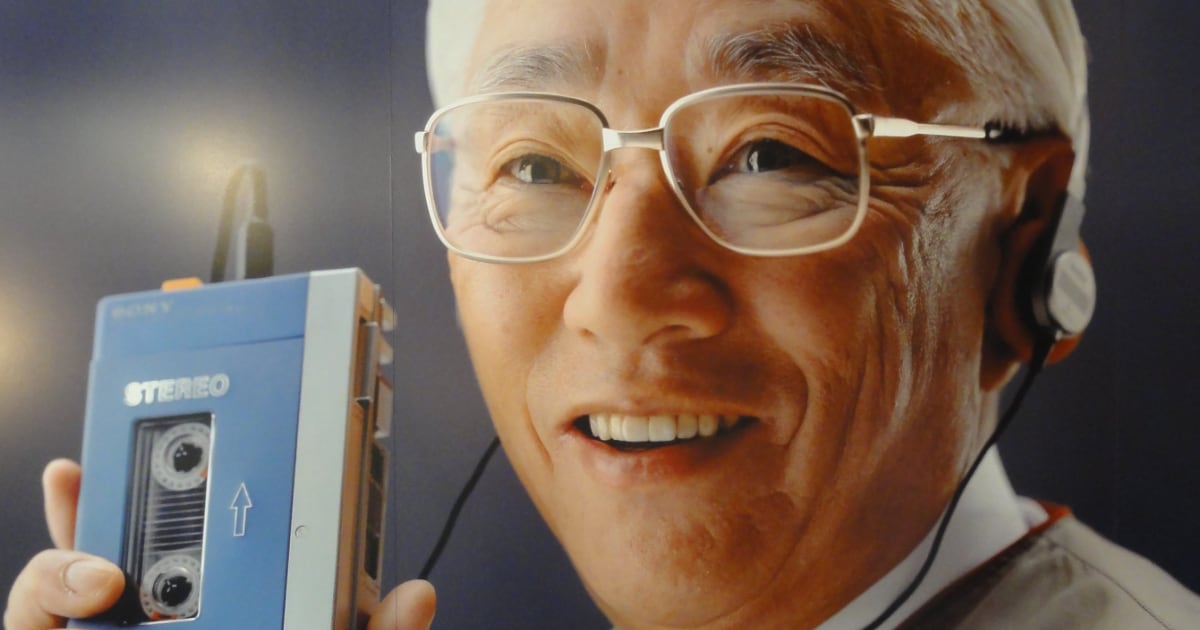 Portrait en gros plan d'Akio Morita, PDG de Sony, portant un casque audio et tenant le premier Walkman TPS-L2 bleu et argent.