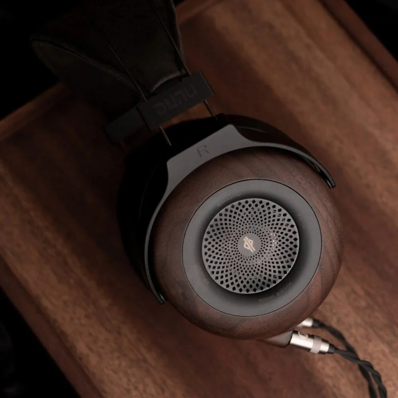 Vue rapprochée de l'oreillette droite du casque DUNU Mortise en noyer noir, montrant la grille d'ouverture centrale et le câble en cuivre monocristallin avec connecteur 3,5 mm.