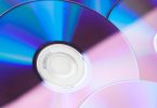Gros plan détaillé sur des compact discs réfléchissants avec des nuances de bleu et de rose, montrant l'anneau central de données.
