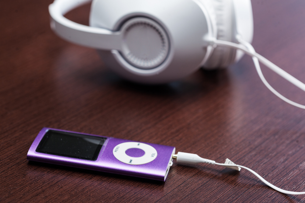 iPod Nano violet de 4e génération branché à un casque audio blanc sur une table en bois sombre.