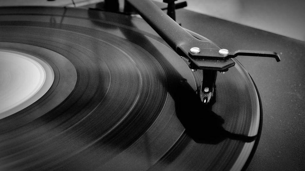 Gros plan artistique en noir et blanc d'un bras de lecture avec pointe de lecture sur un disque vinyle en rotation.