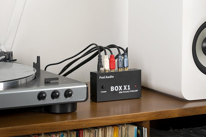 Le préampli phono Fosi Audio BOX X1 est placé dans un environnement intérieur avec une platine vinyle et des enceintes.