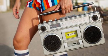 Femme en tenue colorée années 80 tenant un boombox à cassette vintage en plein air
