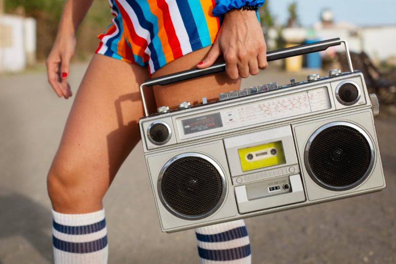 Femme en tenue colorée années 80 tenant un boombox à cassette vintage en plein air