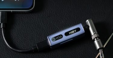 Le HiBy FC3 DAC dongle avec écran OLED posé dans un environnement moderne et lumineux.
