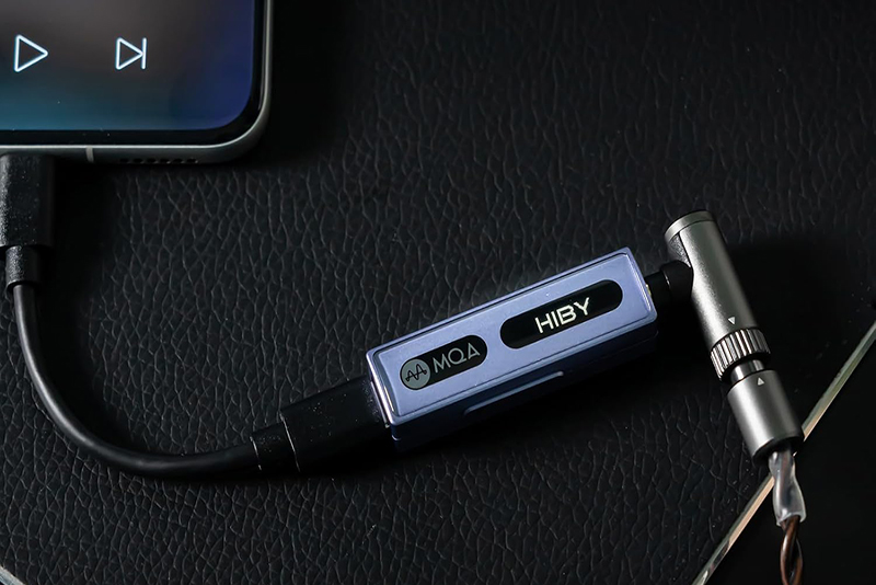 Le HiBy FC3 DAC dongle avec écran OLED posé dans un environnement moderne et lumineux.