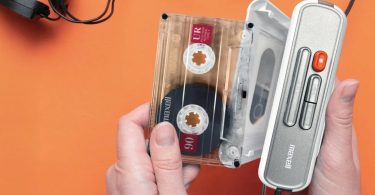 Vue de dessus du lecteur cassette portable Maxell MXCP-P100 blanc et gris, ouvert, avec une cassette Maxell UR 90 insérée sur un fond orange vif.