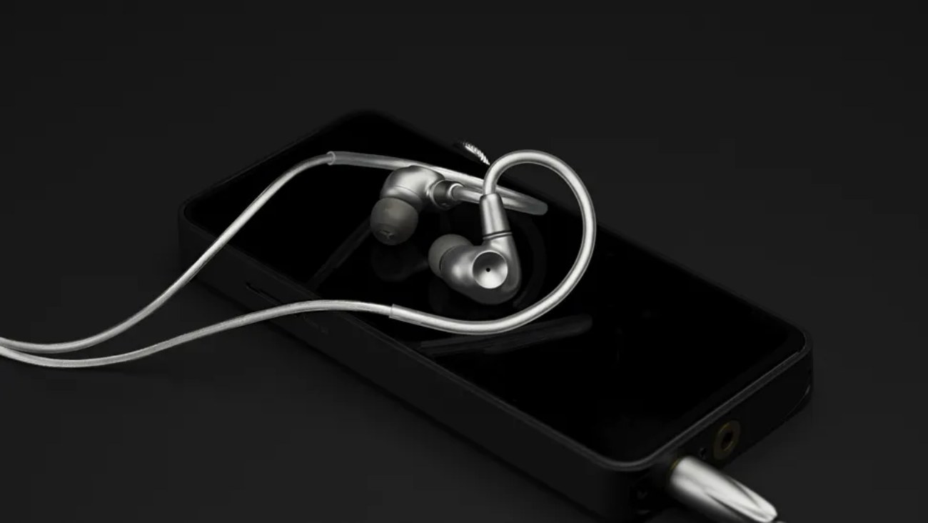 Écouteurs intra-auriculaires Meze Astru en titane posés sur un baladeur numérique noir, connectés via leur câble en aluminium anodisé avec une fiche jack symétrique de 4,4 mm.