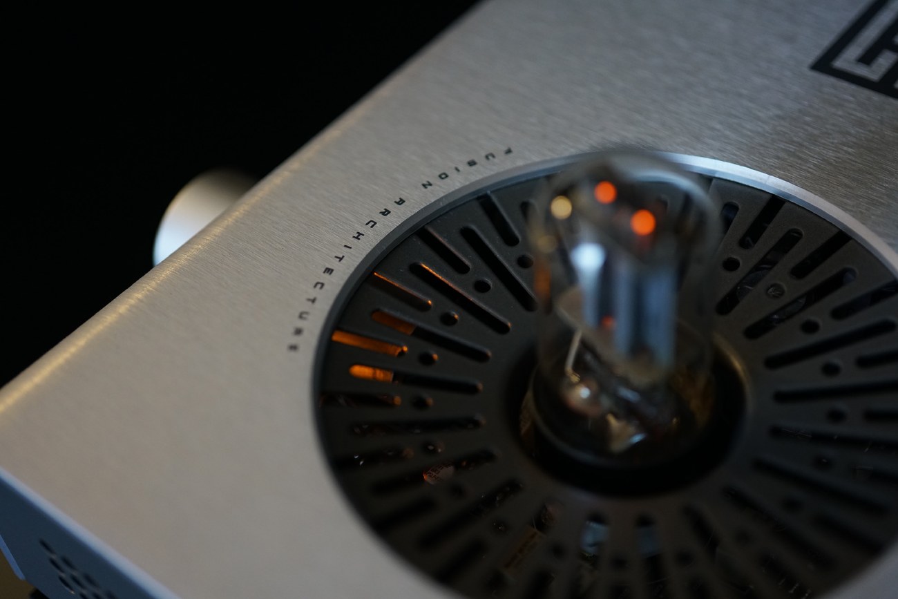 Gros plan sur le tube 6SN7 éclairé au centre de la grille de ventilation du Schiit Lyr 5 argenté, avec l'inscription Fusion Architecture visible sur le châssis en aluminium brossé.