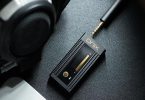 Le dongle DAC SHANLING Onix Alpha XI1 est posé sur une surface avec un casque audio, illustrant son utilisation portable avec un appareil mobile.