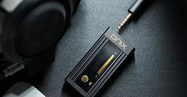Le dongle DAC SHANLING Onix Alpha XI1 est posé sur une surface avec un casque audio, illustrant son utilisation portable avec un appareil mobile.