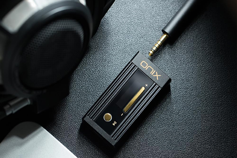 Le dongle DAC SHANLING Onix Alpha XI1 est posé sur une surface avec un casque audio, illustrant son utilisation portable avec un appareil mobile.