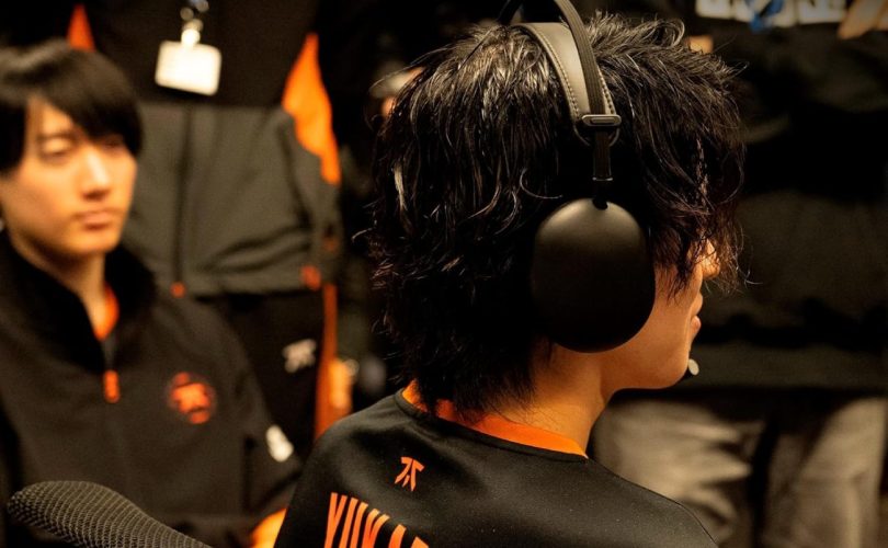Photo de dos d'un joueur d'esport portant le casque Sony InZone H9 II noir. Sa chevelure texturée et l'oreillette noire mate sont bien visibles, avec en arrière-plan flou un coéquipier portant le maillot de l'équipe Fnatic avec des accents orange.