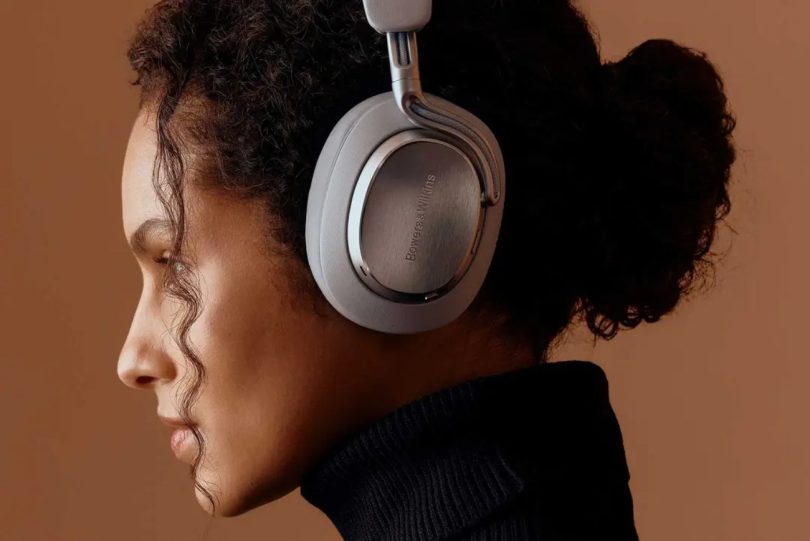 Jeune femme portant le casque sans fil Bowers & Wilkins Px8 S2 en version beige clair avec coques métalliques brossées, fond uniformément coloré terre cuite
