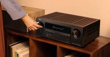 Amplificateur home cinéma Denon AVR-S980H 7.2 canaux posé sur un meuble en bois, avec affichage Dolby Surround Blu-ray