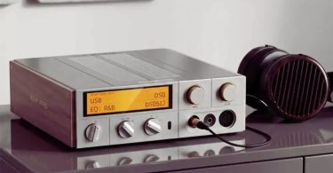 DAC streamer ampli casque FiiO K17 R2R Pro posé sur un meuble laqué prune avec affichage orange montrant USB DSD EQ R&B DSD512, façade argentée avec multiples boutons rotatifs et molette de volume centrale, panneau latéral en bois marqué R2R PRO, présenté avec un casque planar magnétique audiophile