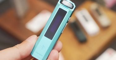 Lecteur audio numérique FiiO Snowsky ECHO NANO en finition turquoise tenu dans une main, avec écran OLED noir et molette de navigation argentée en haut, sur fond de bois flou