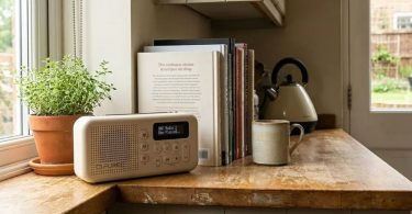Radio portable Pure Elan Move blanche posée sur un plan de travail en bois près d'une fenêtre de cuisine, avec plante aromatique, livres de cuisine et tasse en céramique