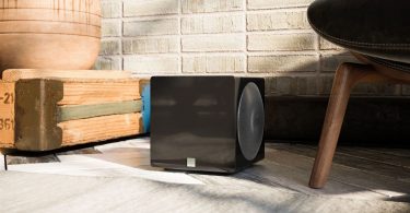 Caisson de basses ultra-compact SVS 3000 Micro R|Evolution en finition noir laqué, installé dans un intérieur moderne à côté d'un fauteuil design.