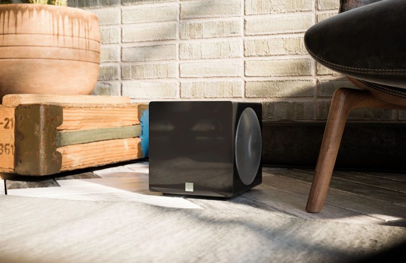 Caisson de basses ultra-compact SVS 3000 Micro R|Evolution en finition noir laqué, installé dans un intérieur moderne à côté d'un fauteuil design.