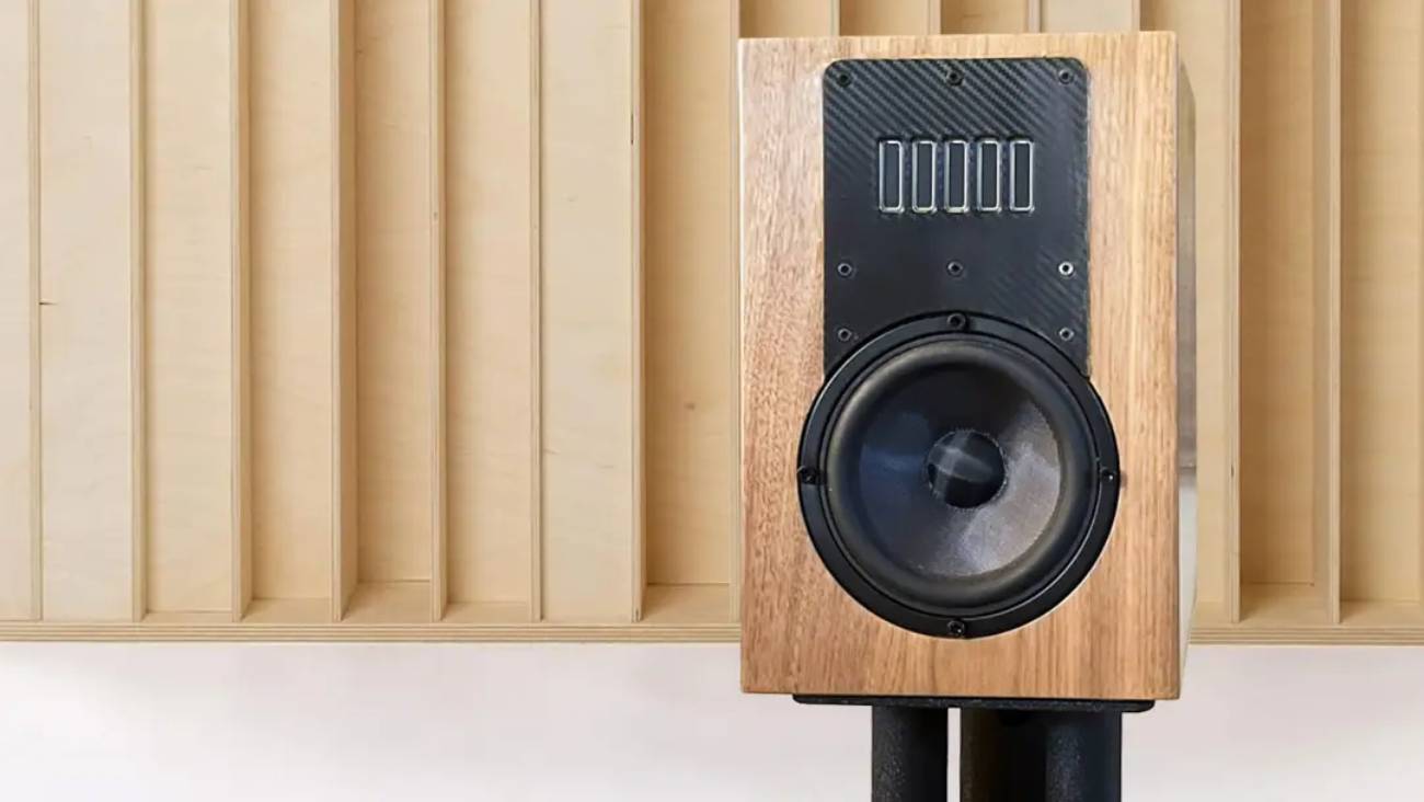 Vue de face frontale du prototype d'enceinte Acoustic3D DaS en ébénisterie noyer naturel, baffle en fibre de carbone twill avec array horizontal de cinq transducteurs AMT à rubans verticaux en partie haute et woofer médium-grave avec phase plug central en partie basse, posée sur stand devant un panneau diffuseur acoustique en bois clair