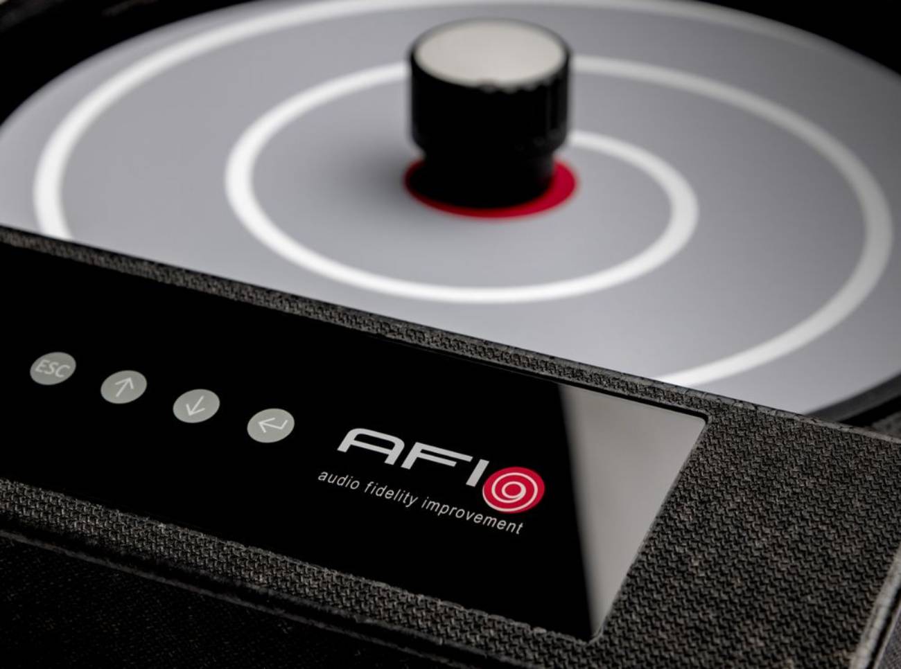 Vue macro de la façade de la AFI Flat.Solo montrant les quatre boutons à actionnement magnétique ESC et flèches directionnelles, le logo AFI Audio Fidelity Improvement avec sa spirale rouge, et en partie supérieure le bed de chargement gris avec cercles concentriques blancs, point central rouge et molette de centrage