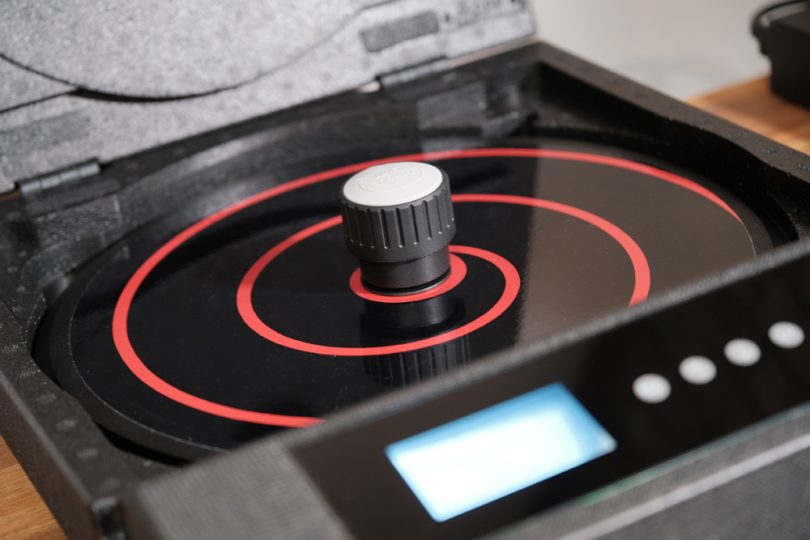 Presse à vinyle AFI Flat.Solo en finition noire mate, couvercle fermé avec logo gris circulaire, écran LCD bleu rétroéclairé affichant les programmes, quatre boutons à actionnement magnétique et logo AFI Audio Fidelity Improvement sur la façade