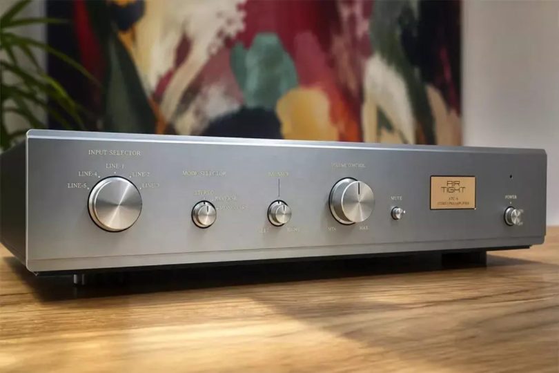 Préamplificateur à tubes Air Tight ATC-6 vu de trois-quarts face en finition argent champagne avec sélecteur Input Selector cinq positions, Mode Selector stéréo reverse mono, contrôle Balance, gros bouton de Volume Control central, sélecteur Mute et plaque dorée signature ATC-6 Stereo Preamplifier sur table en bois clair
