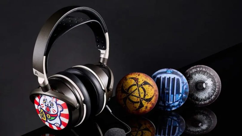 Casque Audeze Maxwell 2 en finition gris anthracite portant une coque ReSkin Kankan Koneko (chat japonais Maneki-neko sur fond rayé rouge et blanc), aux côtés de trois autres coques magnétiques alignées en réflexion sur surface noire laquée : Flux Warning Biohazard jaune, Planar Scan radiographie bleue du driver, et Panopticon All-Seeing Eye