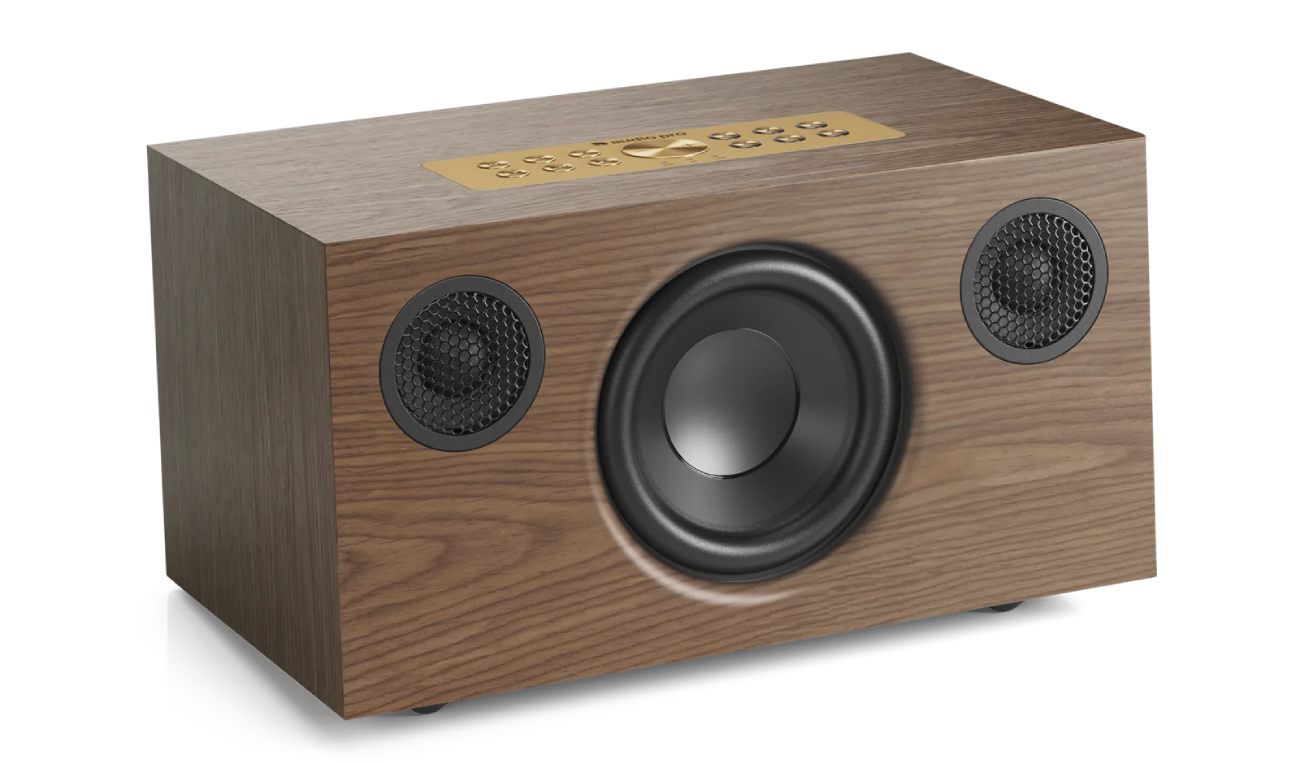 Vue produit catalogue de l'enceinte Audio Pro C5 MkII W Classic en finition placage noyer véritable walnut veneer avec grain naturel parfaitement visible et veines verticales du bois noyer européen, façade épurée sans grille tissu révélant directement le woofer central de 4 pouces et les deux tweeters de 3/4 pouces avec grilles métalliques honeycomb noires, panneau de commande supérieur en métal laiton brass avec six boutons preset, vue trois-quarts perspective sur fond blanc studio neutre