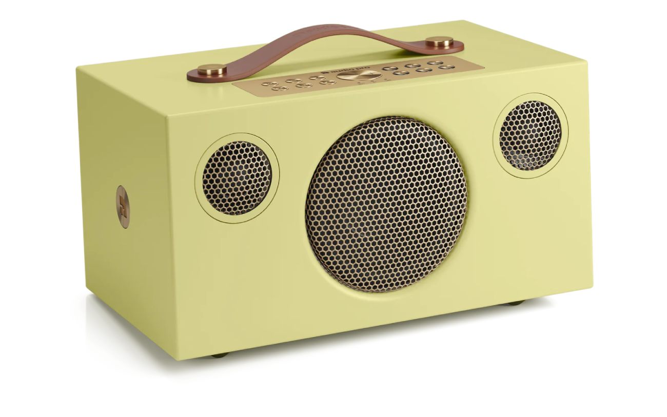 Vue produit officielle catalogue de l'enceinte connectée Audio Pro C5 MkII W Classic en édition limitée jaune pastel avec poignée en cuir véritable cognac et rivets laiton sur le dessus, panneau de commande supérieur en métal couleur laiton brass avec six boutons preset et contrôles de transport, façade épurée sans grille révélant le woofer central de 4 pouces et deux tweeters de 3/4 pouces tous équipés de grilles métalliques laiton à motif nid d'abeille honeycomb, vue de trois-quarts sur fond blanc studio neutre