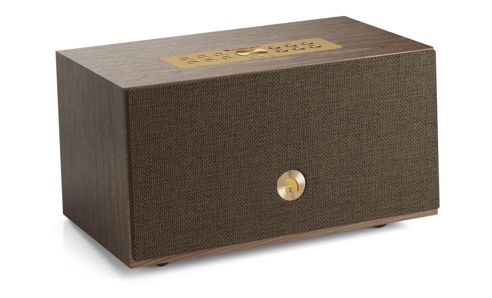 Vue produit catalogue officielle de l'enceinte Audio Pro C5 MkII W standard en finition placage noyer véritable walnut veneer avec grille frontale en tissu marron foncé chocolat couvrant intégralement la façade et bouton circulaire métallique laiton brass au centre, panneau de commande supérieur en métal laiton brass avec six boutons preset et logo audio pro gravé, bordures en bois noyer apparentes sur les arêtes, vue trois-quarts perspective sur fond blanc studio neutre