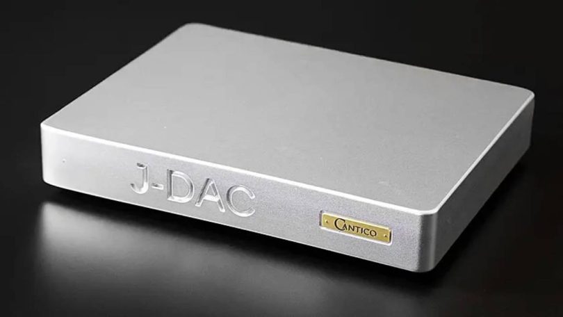 Vue trois-quarts avant du convertisseur numérique-analogique Cantico J-DAC en finition aluminium argent brossé, avec le logo J-DAC gravé en façade et la plaque Cantico dorée caractéristique, châssis unibody fraisé dans la masse de 13 kg sur fond noir