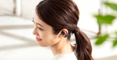 Vue de profil d'une jeune femme portant un écouteur Casio earU ER-100 en finition Navy Black au format open-ear cuff pincé autour du pavillon de l'oreille gauche, sans obstruction du conduit auditif, lumière naturelle douce et arrière-plan végétal flouté