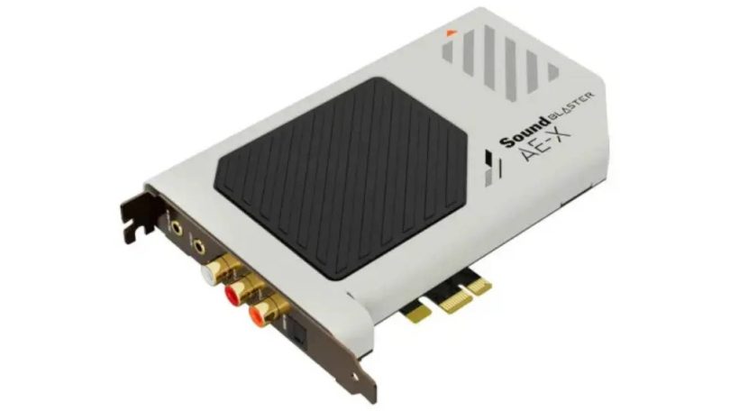 Carte son interne Creative Sound Blaster AE-X en finition blanche vue de trois-quart, montrant le dissipateur central hexagonal noir, le logo Sound Blaster AE-X, le connecteur PCIe 3.0 x1 et la connectique arrière avec jacks 3,5 mm, RCA L/R dorés et port optique TOSLINK
