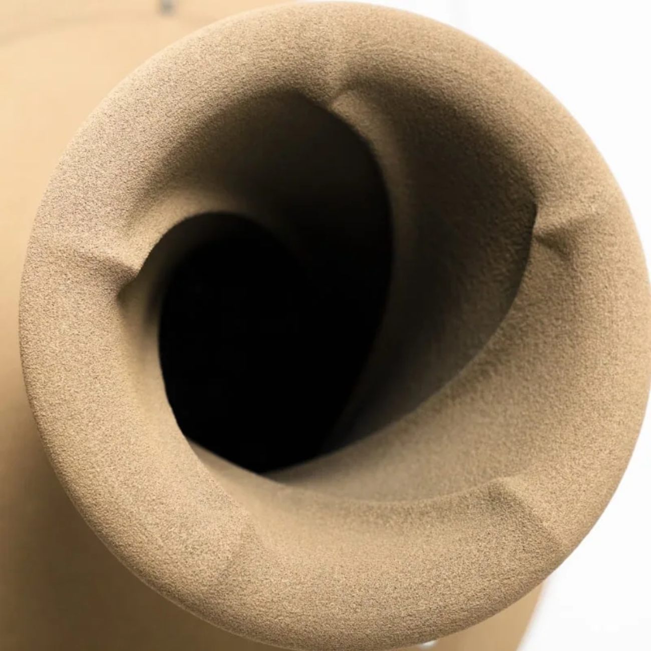Détail macro de l'évent basse-réflex arrière en forme de buse de l'enceinte active Econik 1851, intégré directement dans la sphère grave en sable de quartz imprimé 3D imprégné d'époxy, ouverture circulaire évasée vers l'intérieur de la chambre acoustique, texture minérale rugueuse caractéristique en finition naturelle ton sable