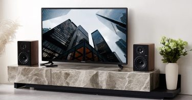 Paire d'enceintes actives Elipson Prestige Facet II 6 Active BT en finition noyer encadrant un téléviseur Samsung sur meuble en marbre, illustrant l'usage HDMI ARC en salon contemporain