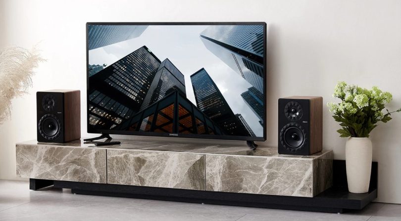 Paire d'enceintes actives Elipson Prestige Facet II 6 Active BT en finition noyer encadrant un téléviseur Samsung sur meuble en marbre, illustrant l'usage HDMI ARC en salon contemporain