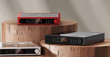 Trois FiiO DM15 R2R lecteurs CD portables présentés côte à côte en finitions rouge, noir et argent, écrans LCD allumés affichant le mode CD, posés sur des socles en bois brut