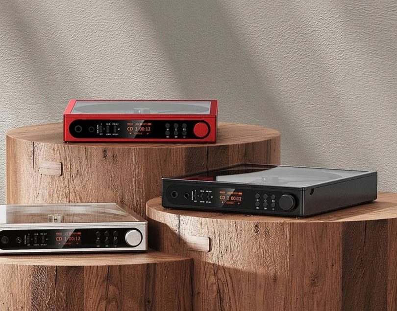 Trois FiiO DM15 R2R lecteurs CD portables présentés côte à côte en finitions rouge, noir et argent, écrans LCD allumés affichant le mode CD, posés sur des socles en bois brut
