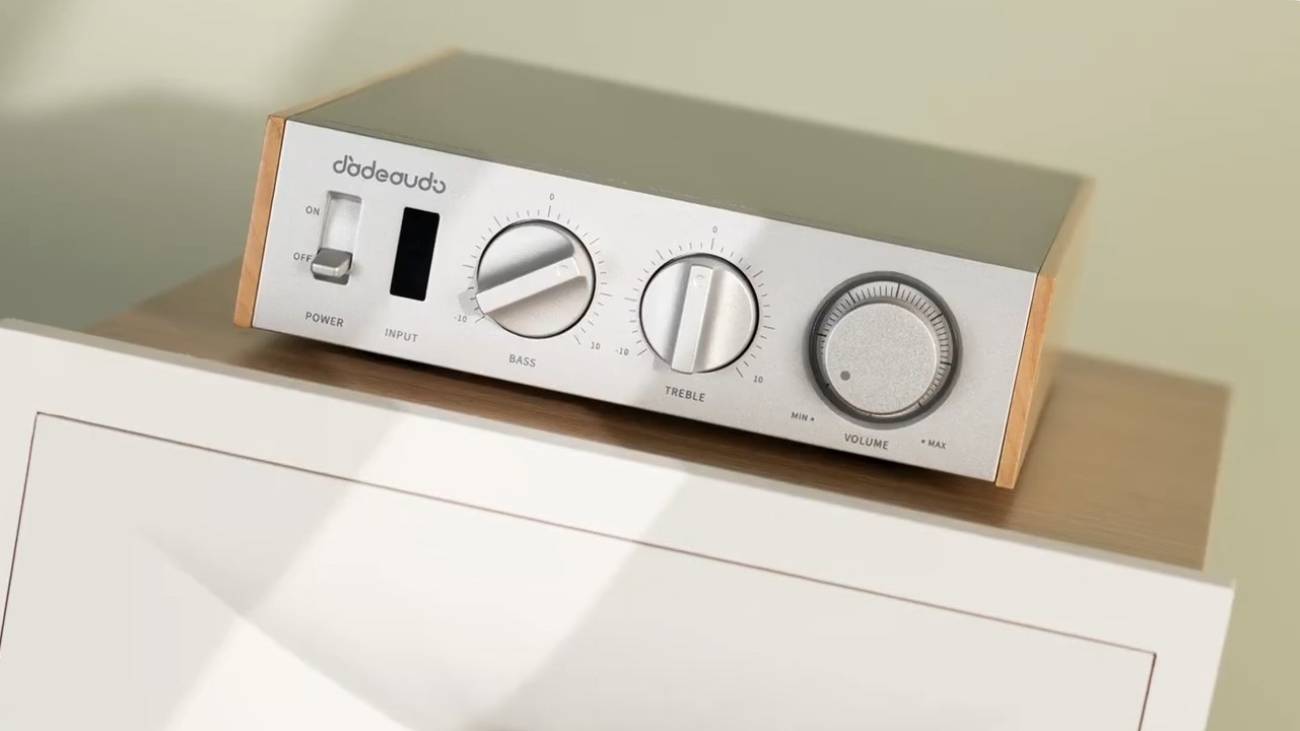 Façade du FiiO Jade Audio LEVEL 1 en finition argent à flancs en bois clair, posé sur un meuble blanc : interrupteur POWER à bascule, fenêtre INPUT, molettes BASS et TREBLE graduées et gros bouton de VOLUME, logo Jade Audio