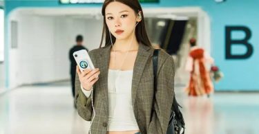 Une utilisatrice en aéroport tient son smartphone équipé du DAC portable Fosi Audio MD3 MagDac fixé magnétiquement au dos, écran circulaire visible, IEM filaires connectés à la sortie casque pour écouter de la musique en haute résolution en déplacement.