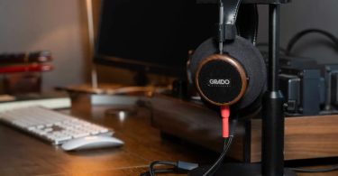 Casque audiophile Grado Signature S550 ouvert avec coque ronde en noyer brésilien massif et logo GRADO blanc, posé sur un support de casque à côté d'un setup de bureau, câble détachable Silver rouge et noir visible