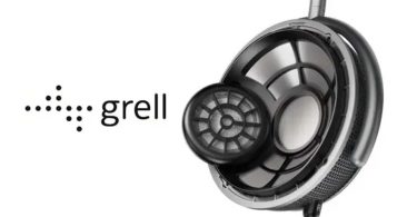 Casque circumaural Grell Audio en finition noire et argent vue de trois quarts en gros plan, transducteur principal circulaire à grille structurée en spirale géométrique visible à travers la coque ajourée, second transducteur de plus petit diamètre positionné en diagonale en avant de l'oreille caractéristique de la technologie FSFM Front Side Sound Field Modulation, arceau métallique gris foncé courbé, coussinet noir mat, marquage R indicateur canal droit visible, câble noir descendant à la base, grille de ventilation acoustique sur la tranche inférieure, logo de la marque grell en typographie minuscule sans empattement accompagné de son indicateur visuel à 26 points alignés en flèche horizontale vers la droite, fond blanc neutre