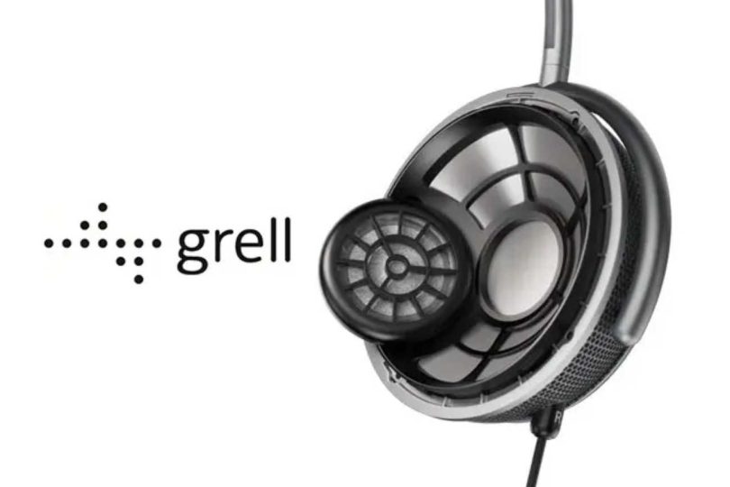 Casque circumaural Grell Audio en finition noire et argent vue de trois quarts en gros plan, transducteur principal circulaire à grille structurée en spirale géométrique visible à travers la coque ajourée, second transducteur de plus petit diamètre positionné en diagonale en avant de l'oreille caractéristique de la technologie FSFM Front Side Sound Field Modulation, arceau métallique gris foncé courbé, coussinet noir mat, marquage R indicateur canal droit visible, câble noir descendant à la base, grille de ventilation acoustique sur la tranche inférieure, logo de la marque grell en typographie minuscule sans empattement accompagné de son indicateur visuel à 26 points alignés en flèche horizontale vers la droite, fond blanc neutre