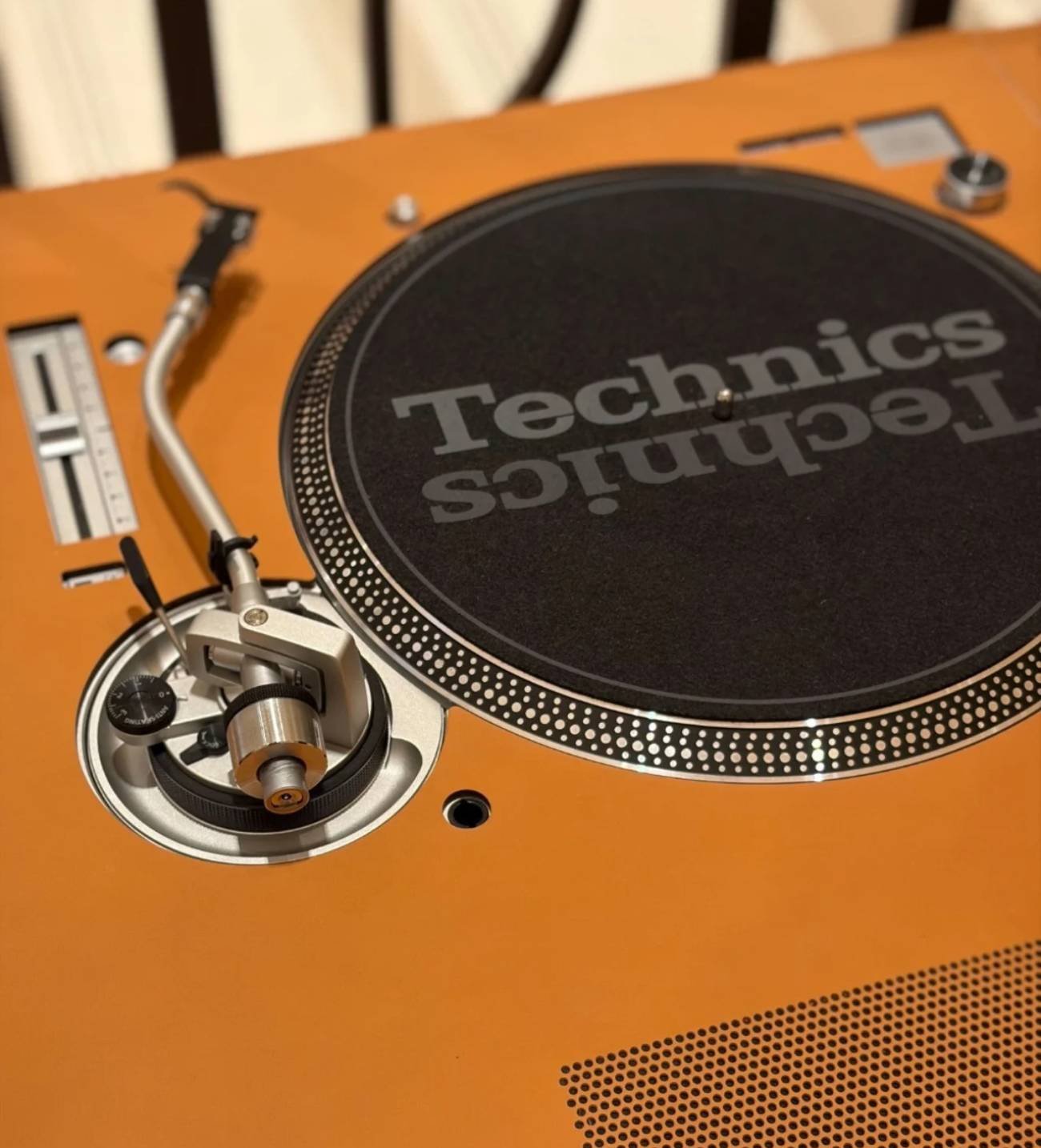 Gros plan de la platine Technics intégrée à la table de DJ Hermès Disque Jockey Club : tapis de feutre marqué Technics, bras de lecture en S argenté, pitch fader, points stroboscopiques et dispositif d'anti-skating, le tout encastré dans une surface en cuir fauve perforé