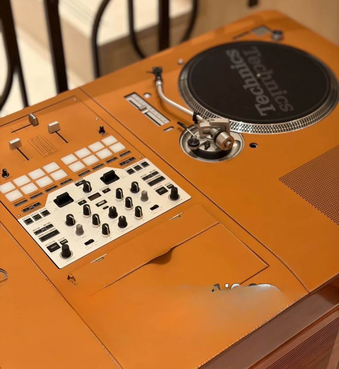 Gros plan du plateau de la table de DJ Hermès Disque Jockey Club : platine vinyle Technics au bras en S à droite, table de mixage à boutons argentés et pads de performance à gauche, surface entièrement habillée de cuir de vachette Pippa surpiqué de teinte fauve