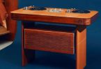 Table de DJ Hermès Atelier Horizons Disque Jockey Club en acajou verni, avec deux platines vinyle japonaises et une table de mixage centrale exposées sur le plateau, panneau frontal habillé de cuir, posée sur fond bleu dans un intérieur contemporain