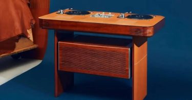 Table de DJ Hermès Atelier Horizons Disque Jockey Club en acajou verni, avec deux platines vinyle japonaises et une table de mixage centrale exposées sur le plateau, panneau frontal habillé de cuir, posée sur fond bleu dans un intérieur contemporain
